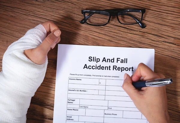 Slip and fall accident report being filled out beside an injured wrist in a cast