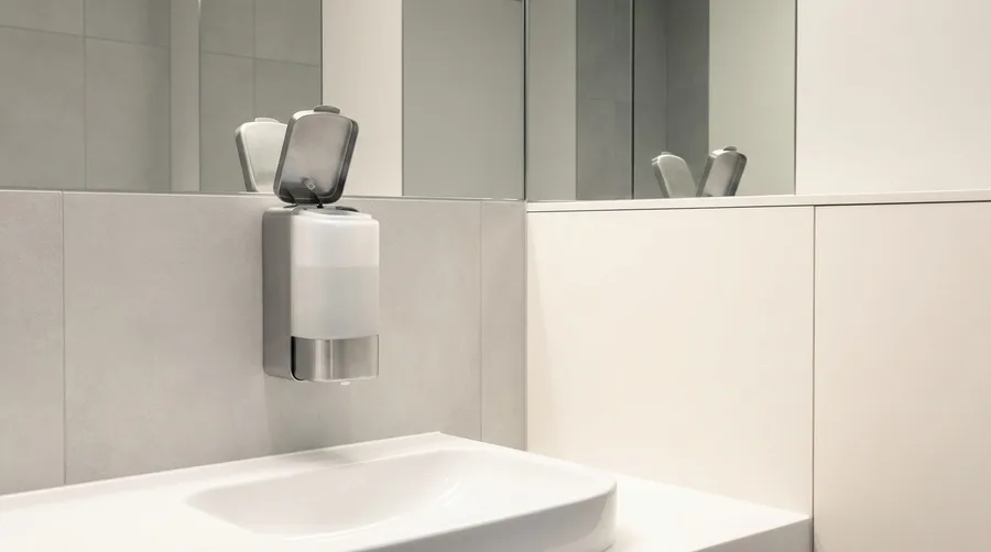 An open, empty wall-mounted soap dispenser in an office restroom