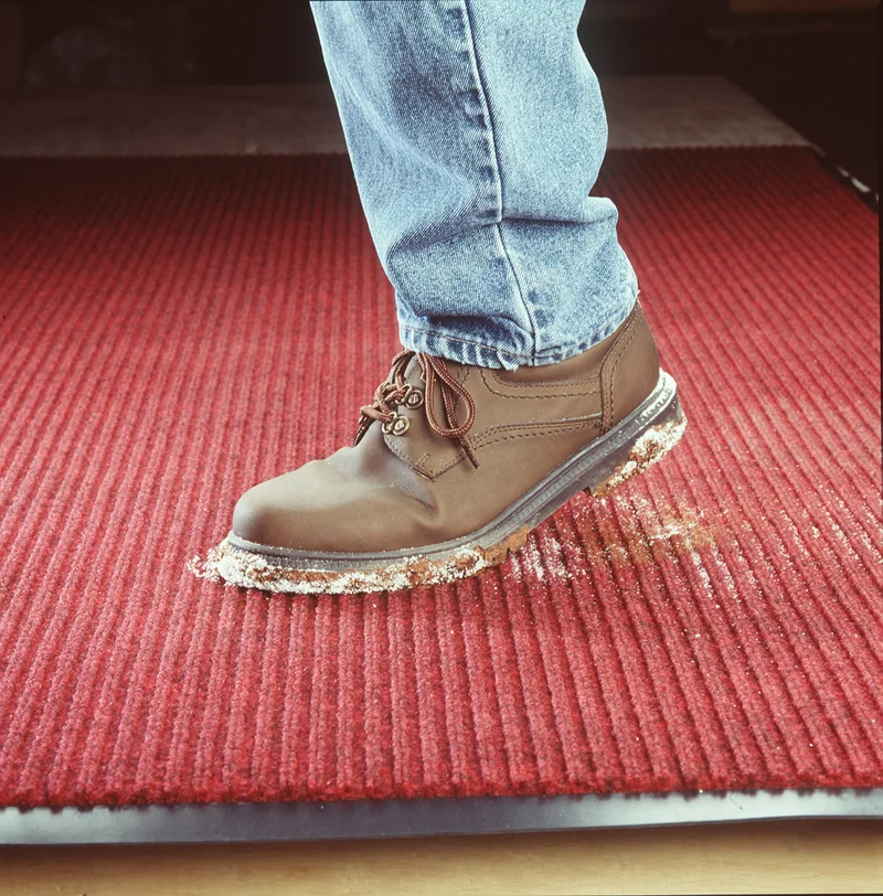 Work boot shedding dirt onto a ribbed scraper mat