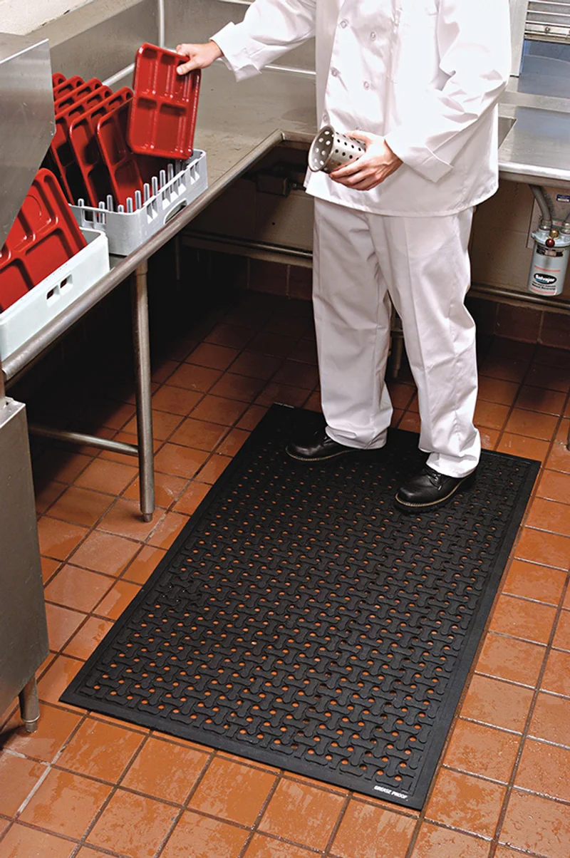 Commercial utility mat with drain channels in use at a kitchen dish station